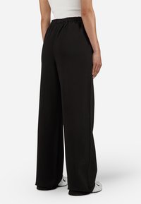 Black wide-leg pants with an elastic waistband, made of soft fabric. The hem touches the footwear, showcasing a casual design.