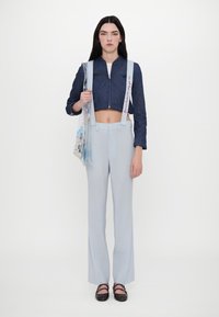 Izrezana jeans jakna z vezenjem v obliki srca, kombinirana s svetlo modrimi elegantnimi hlačami in okrašeno prozorno torbo z grafiko.