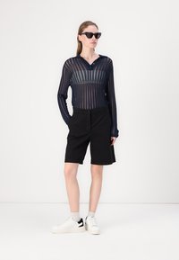 Top lungo a maniche zero in velluto navy con righe verticali, pantaloni corti neri fino al ginocchio e sneakers bianche con dettagli neri. Design minimalista, vestibilità casual.