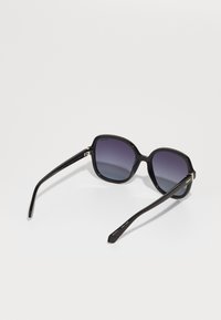 Black oversized sunglasses with gradient purple lenses. Smooth plastic frame with gold accents on the side and sleek black temples.