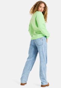 Sudadera verde claro con puños acanalados, combinada con jeans baggy azul claro que tienen un acento en forma de corazón en el bolsillo trasero.