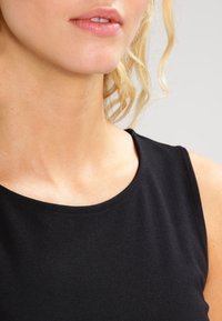 Černý bezramínkový top s kulatým výstřihem, vyrobený z hladké látky. Ukazuje kůži na krku a klíční kosti, bez výrazných vzorů nebo akcentů.