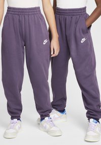 Lila melegítőnadrág, elasztikus derékpánttal és szegélyekkel. Oldalsó zsebekkel és fehér Nike logóval a bal comb felső részén. Puha, bolyhos anyag.