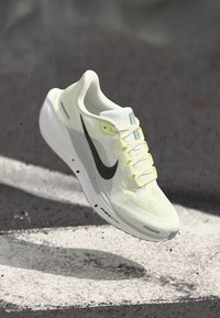 Baskets de course jaune clair avec tige en maille, semelle blanche et logo swoosh noir, présentant un design à lacets et une texture respirante.