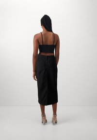Jupe midi en denim noir à coupe droite, avec poches arrière et une fente. Associée à un top court noir et des sandales à talons transparents.