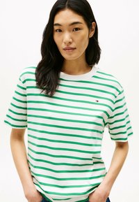 Camiseta de manga corta a rayas verde y blanca, con cuello redondo y un pequeño logo en el pecho, fabricada en tela de algodón.
