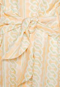 Lehké šaty zavinovací ze soft žluté látky se zeleným a bílým cikcak vzorem. Mají zavázání v pase a splývavý vrstvený design.