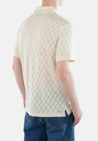 Kortermet polo skjorte i off-white med diamantstrikk mønster, ribbestrikket krage, sidesplitter og liten logo aksent nær kanten.