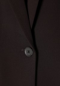 Dark brown blazer fabric with smooth texture. Features a prominent black button with a 4-hole design, situated near the lapel.