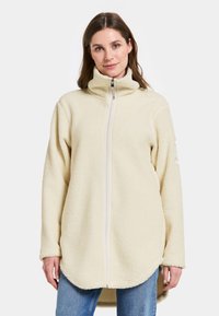 Crème-kleurige fleece jack met een hoge kraag en volledige rits. Heeft een zachte textuur en een gebogen zoomlijn. Geaccentueerd met een merlogo op de mouw.