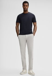 T-shirt bleu marine à col rond associé à un pantalon gris clair. Le modèle porte des baskets beige. Les tissus semblent doux et confortables, avec une texture lisse.