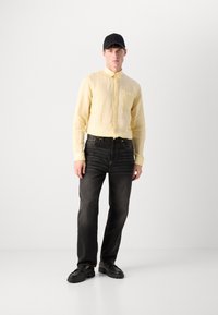 Yellow linen button-up shirt, black denim jeans, black shoes with thick soles, and a black cap. Simple design, lightweight texture.