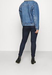 Jeansjacka med en fårskinnskrage, avslappnad passform, ljusblå färg. Kombinerad med mörka tajta jeans och ankelstövlar. Bakifrån.