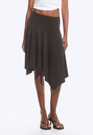 Femme portant une jupe noire asymétrique mi-longue associée à des sandales à talons noires et un top court blanc.