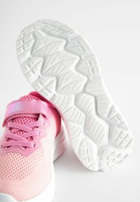 Baskets de sport roses avec une tige en mesh, des superpositions texturées et une semelle extérieure en caoutchouc blanc avec un design de grip patterné. Sangle Velcro sur le dessus.