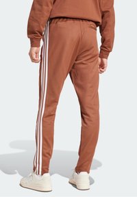 Bruna träningsbyxor med vita sidostygn, elastisk midja och smalnade ben. Har en bakficka och mjukt, texturerat tyg.