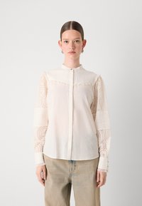 Camicia bianca con bottoni, in tessuto testurizzato e dettagli in pizzo sulle maniche, caratterizzata da un colletto rotondo e una vestibilità leggermente rilassata.