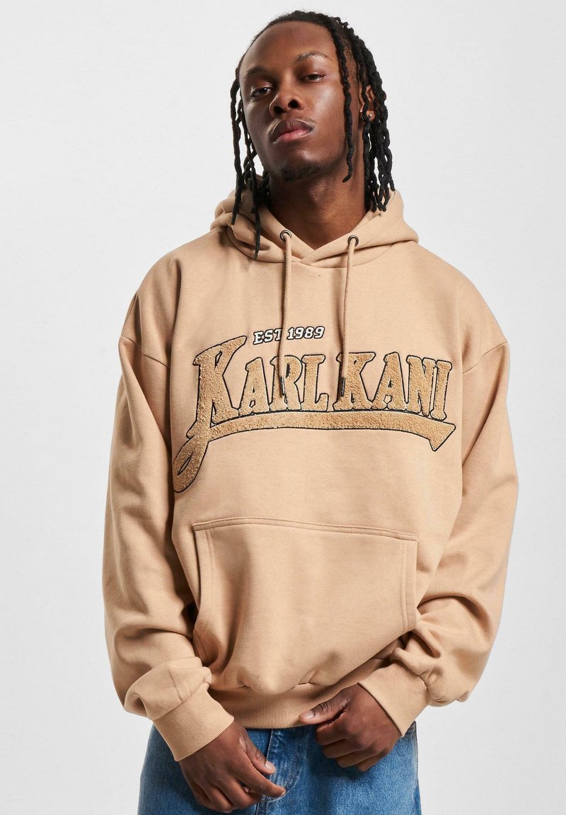 Bežinė džinsinė striukė su priekinėmis kišenėmis, su ryškiu „KARL KANI“ grafiniu ženklu ir „EST 1989“ tekstu juoda ir auksine spalvomis. Minkšta, tekstūruota medžiaga.