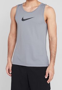 Camiseta deportiva sin mangas gris, hecha de tela ligera, con cuello redondo y un logo negro de Nike en el pecho.