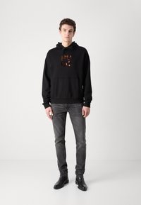 Sudadera con capucha negra con un logo "HUGO" brillante en color metálico oscuro; bolsillo canguro; combinada con jeans grises y botas de cuero negras.