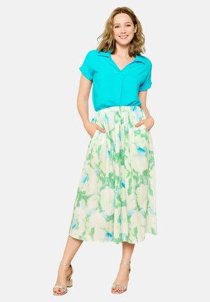 Blusa turchese a maniche corte abbinata a una lunga gonna bianca fluida con motivi ad acquerello verdi e blu; include tasche laterali.