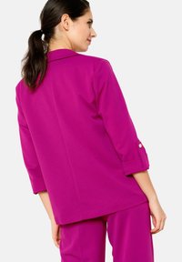 Blazer fucsia con un design su misura, maniche a tre quarti e dettagli con bottoni dorati, realizzato in tessuto liscio, mostrato da dietro.