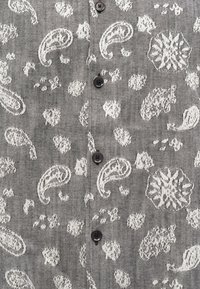 Hallhalli hallide ja lillemustriga hall kangas särk, millel on mustad nööbid ees, tekstureeritud kude ja keerukad detailid.