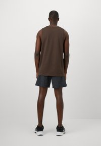 Camisa castanha sem mangas com um corte descontraído, combinada com calções cinza escuro. A pessoa está a usar ténis de desporto pretos.