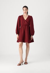 Rochie burgundy cu maneci lungi puff, talie strânsă și fustă evazată. Textură netedă. Asortată cu pantofi cu vârf deschis de culoare maro, cu accente.
