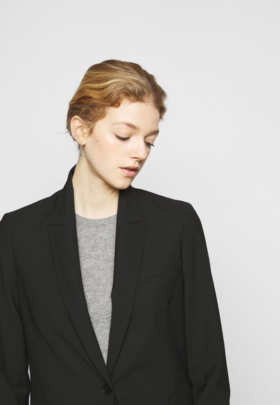 Blazer preto com um corte ajustado, apresentando colarinho com lapelas e fecho de um único botão, sobreposto a um suéter cinza claro. Textura de tecido suave.