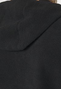 Zwarte fleece hoodie met een zachte textuur, voorzien van een capuchon en nette naden, die warmte en comfort benadrukken. Geen logo's of extra details zichtbaar.