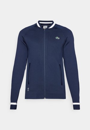 Morski zip-up jakna s bijelim i plavim prugastim ovratnikom i manžetama, dva prednja džepa i mali вышит логотип na prsima.