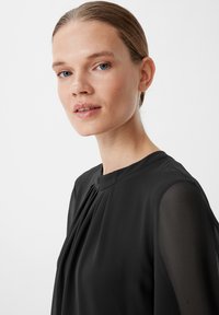 Czarna bluzka o wysokim dekolcie, z plisowanym przodem i przezroczystymi długimi rękawami. Gładka faktura z subtelnym drapowaniem, oferująca elegancki wygląd.