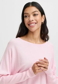 Pull léger rose avec un large décolleté et des manches longues, comprenant des poignets côtelés. Texture lisse, coupe décontractée, détails minimaux.