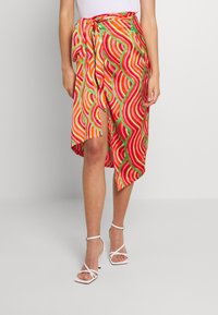 Jupe portefeuille colorée présentant un motif ondulé en rouge, orange, rose et vert, avec une fente latérale et un détail à nouer à la taille.