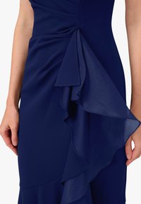 Navyblaues Kleid mit drapiertem Rüschendetail an der Seite, aus weichem Stoff mit glatter Textur und taillierter Silhouette.