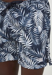 Marinblå badshorts med ett mönster av vita och ljusblå palmlöv, utrustade med elastisk midja och dragsko för justerbar passform.