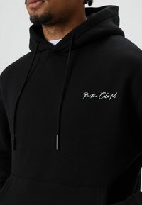 Zwarte hoodie met trekkoord, voorzien van een wit sierlijk logo "Pantone Colorful" op de borst. Gemaakt van zachte, gestructureerde stof.