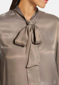 Zijdeachtig taupe blouse met een vastgebonden strik in de kraag. Heeft een gladde textuur en een lichtgewicht ontwerp, wat een verfijnde uitstraling biedt.