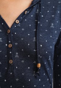 Marineblauwe hoodie met houten knopen en trekkoorden, voorzien van kleine witte weer- en geometrische patronen op zachte stof.