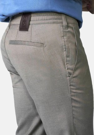 Nahaufnahme einer Person, die hellgraue Hosen mit einer Gesäßtasche und einem Lederpatch mit der Aufschrift "M5" am Bund trägt.