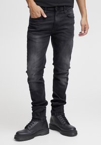 Slim-fit zwarte jeans met een vervaagde textuur, vijf zakken en riemlussen, gecombineerd met zwarte veterschoenen met een chunky zool.
