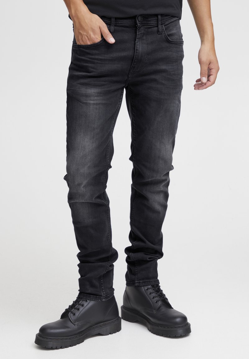 Slim-fit zwarte jeans met een vervaagde textuur, vijf zakken en riemlussen, gecombineerd met zwarte veterschoenen met een chunky zool.
