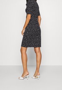 Svart klänning med prickar, korta puffärmar, figursydd design, midjängd fåll; kombinerad med vita öppna tå-hälskor.