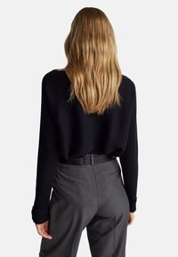 Czarny sweter prążkowany o luźnym kroju i długich rękawach, zestawiony z szarymi spodniami o dopasowanym kroju z gładkiej tkaniny oraz czarnym paskiem.