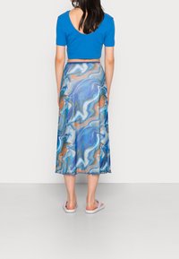 Niebieski crop top z okrągłym tyłem, zestawiony z długą, zwiewną spódnicą o marmurkowym wzorze w odcieniach niebieskiego, pomarańczowego i białego, noszoną z fioletowymi sandałami.