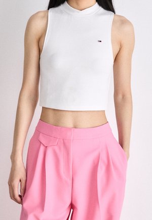 Biały krótki top bez rękawów z wysokim kołnierzem, z małym logo na piersi. Do tego różowe spodnie z wysokim stanem i kieszeniami.