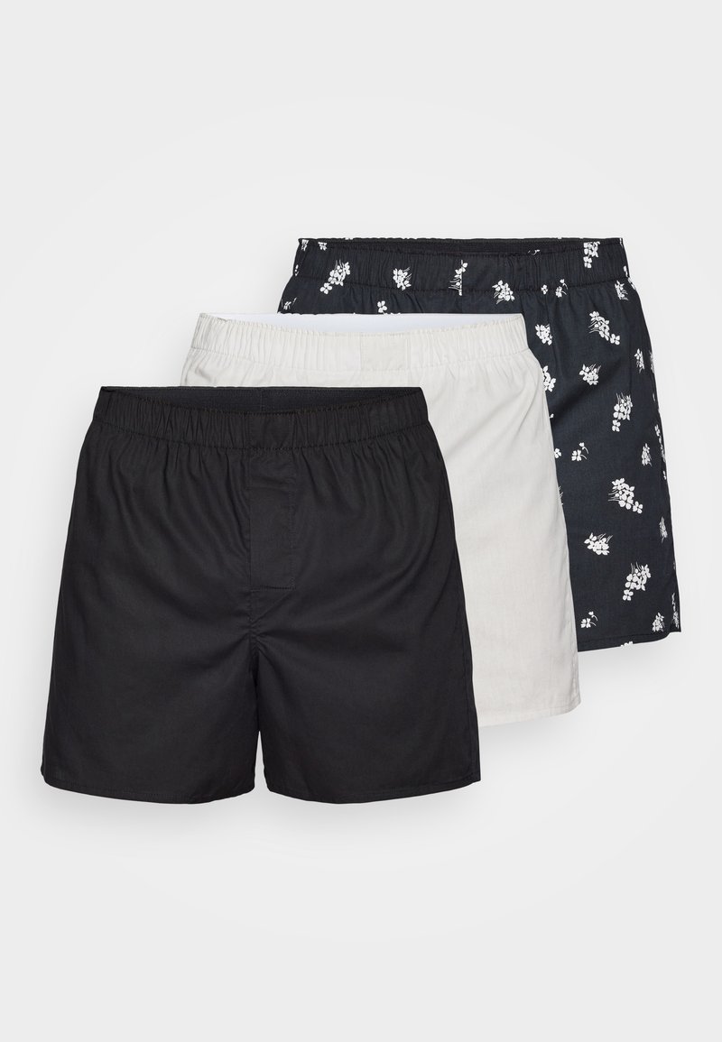 Zestaw trzech par szortów: jedne czarne, jedne białe i jedne w wzór granatowy w białe kwiaty, wszystkie z elastycznymi pasami i lekkim materiałem.