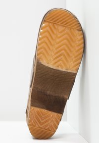 Chaussure en cuir marron avec une surface texturée, affichant une semelle en caoutchouc. La semelle présente un motif en chevrons pour une meilleure adhérence.