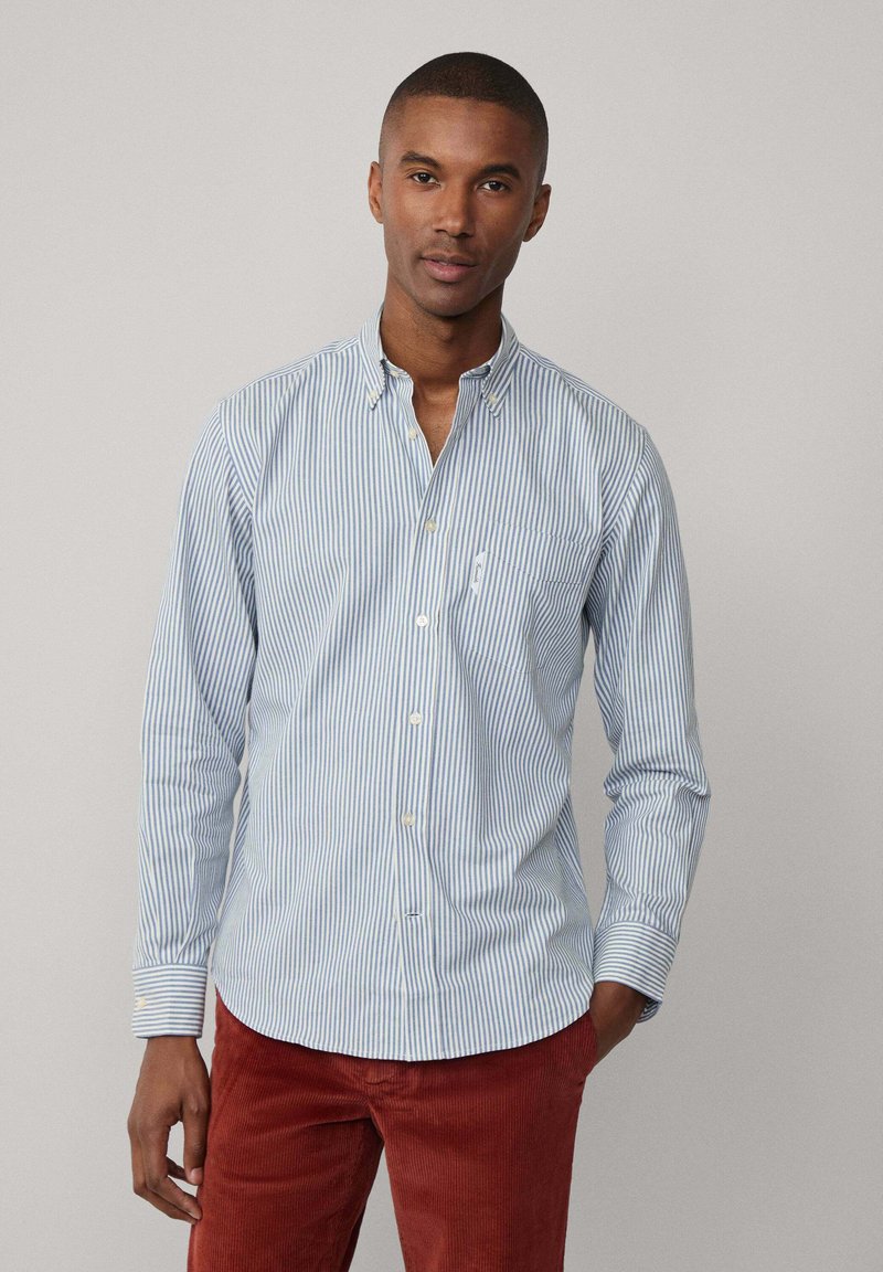 Camisa a rayas azul claro y blanca con mangas largas, collar abotonado y bolsillo en el pecho. Fabricada en algodón con una textura suave.
